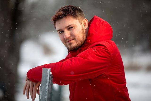 Marius Bråtelund lener seg over et gjerde. Han har rød anorakk, det er snø i bakgrunnen.
